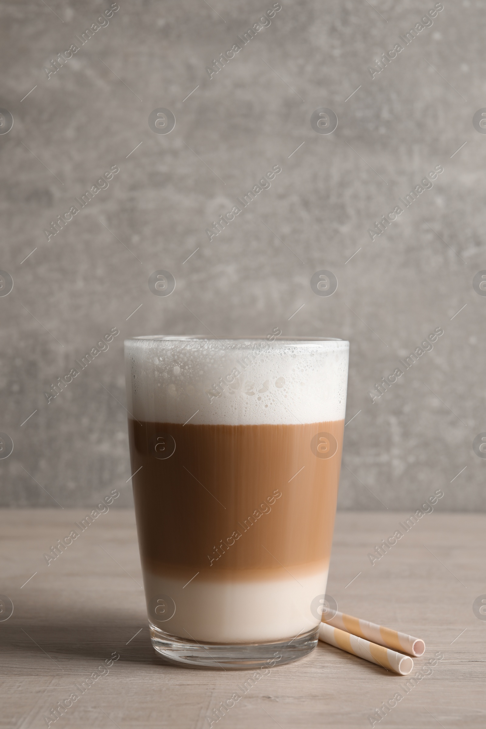 Photo of Glass of delicious layered coffee and straws on wooden table against light grey background, space for text