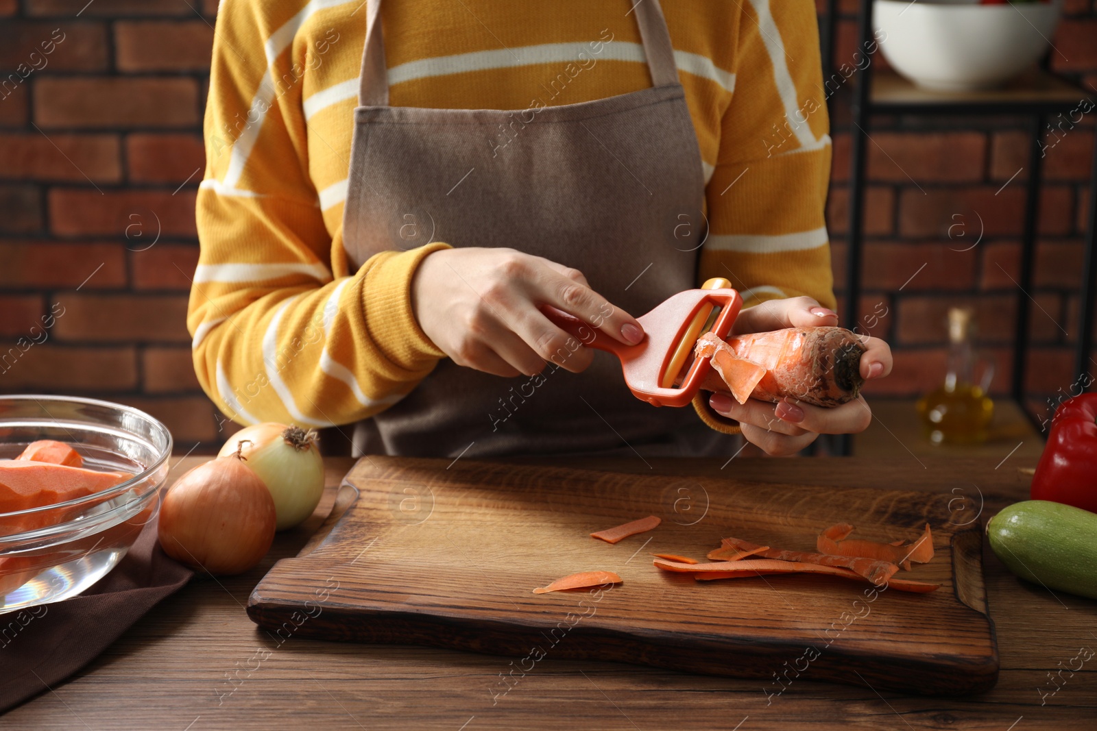 Photo of Woman peeling fresh carrot at wooden table indoors, closeup