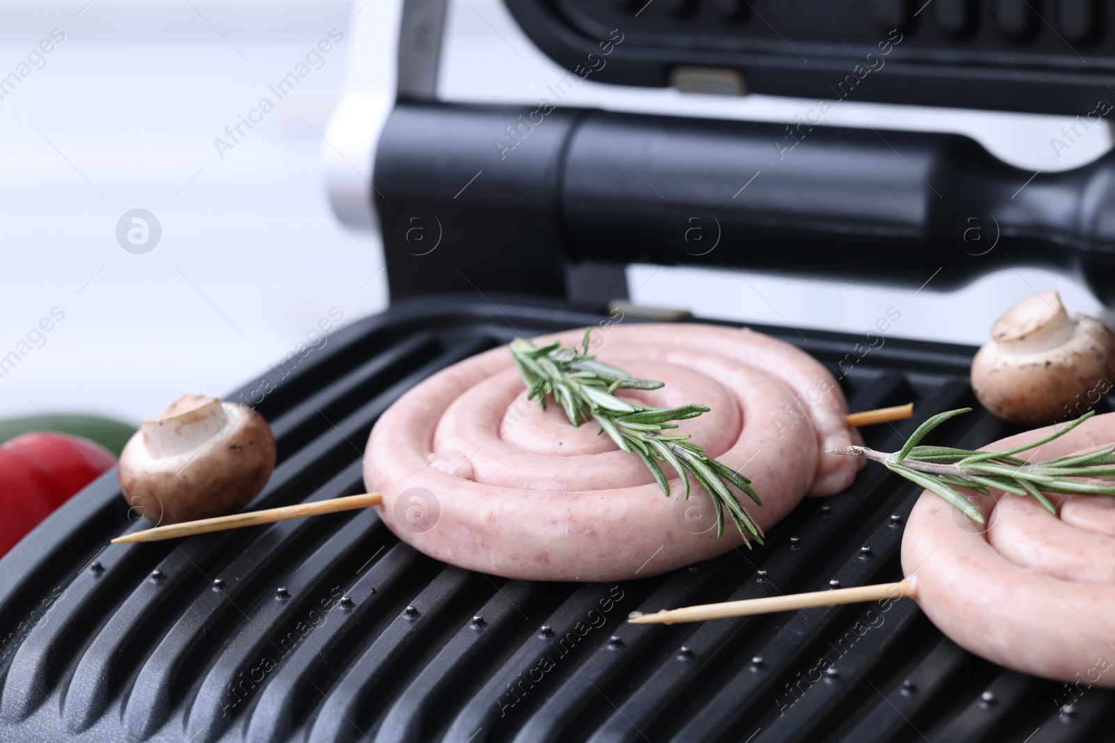 Photo of Homemade sausages, mushrooms and rosemary on electric grill, closeup