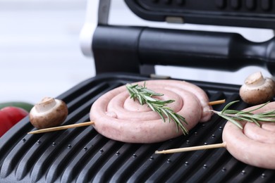 Photo of Homemade sausages, mushrooms and rosemary on electric grill, closeup