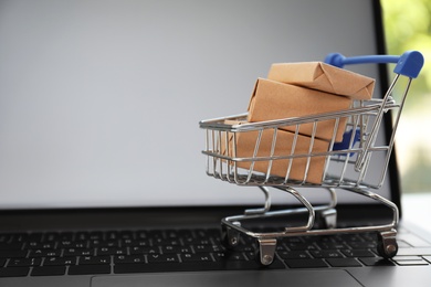 Internet shopping. Small cart with boxes on modern laptop, space for text