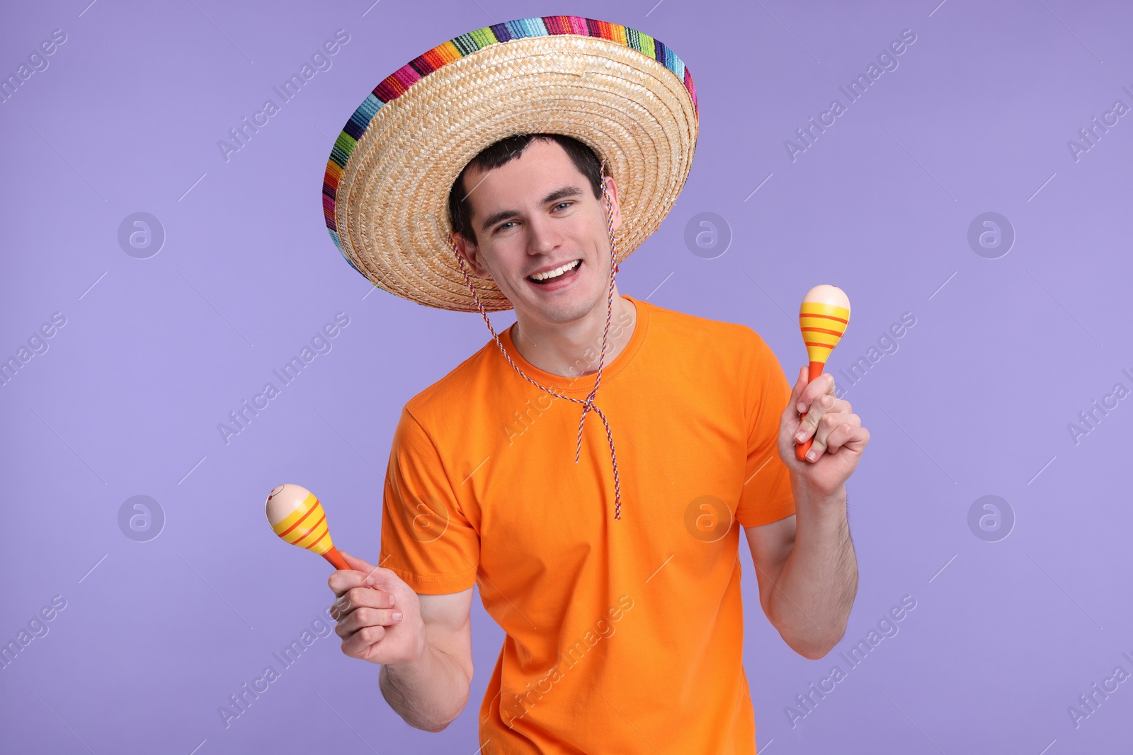 Photo of Young man in Mexican sombrero hat with maracas on violet background