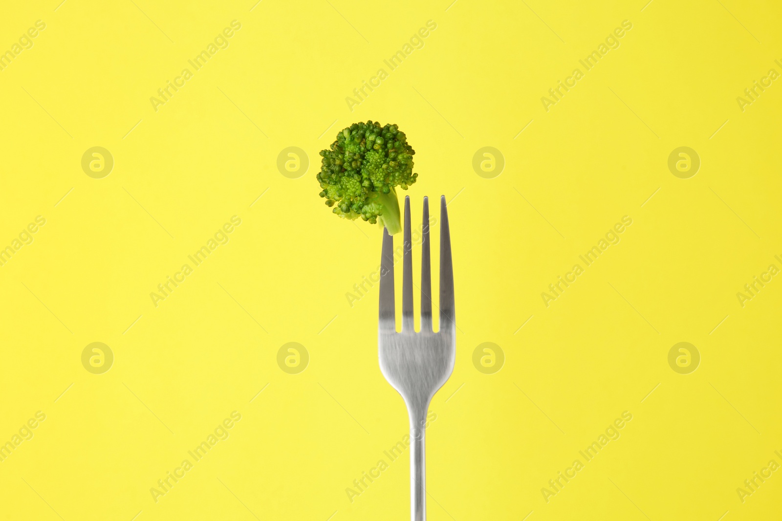 Photo of Fork with tasty broccoli on yellow background