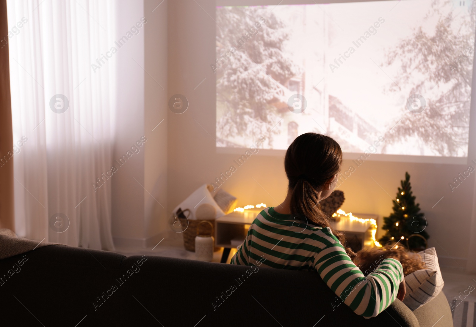 Photo of Mother and son watching Christmas movie via video projector at home, back view