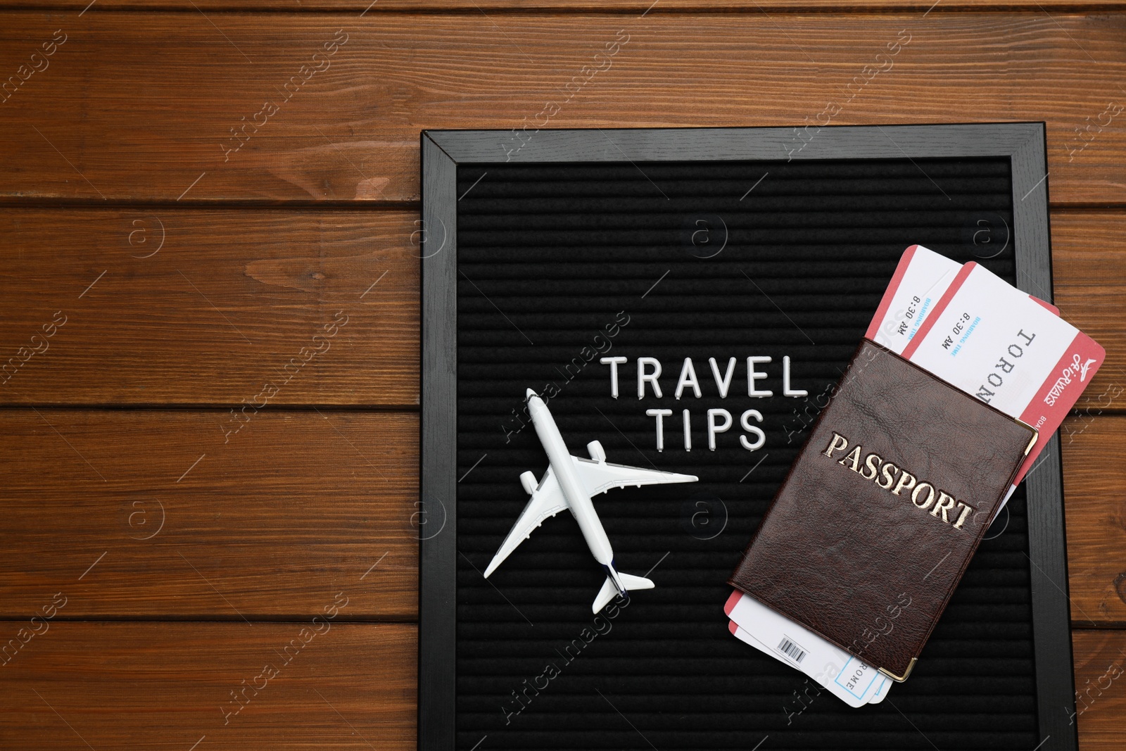 Photo of Black letter board with phrase Travel Tips, passport, tickets and toy plane on wooden table, top view. Space for text