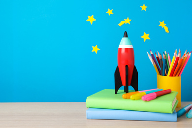 Photo of Bright toy rocket and school supplies on wooden desk. Space for text