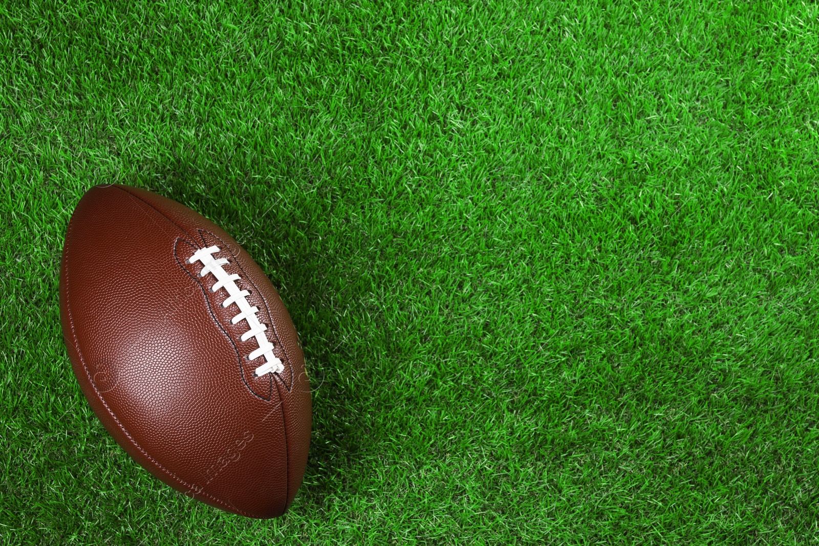 Photo of American football ball on green grass, top view. Space for text