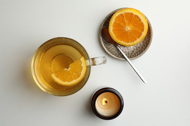 Photo of Cup of freshly brewed tea, burning candle and orange on light table, flat lay