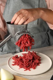 Woman making beef mince with manual meat grinder at light wooden table, closeup