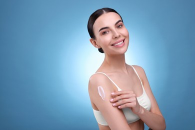 Photo of Beautiful woman with smear of body cream on her shoulder against light blue background, space for text