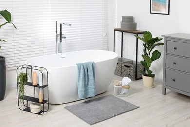 Stylish bathroom interior with bath tub, houseplants and soft light grey mat