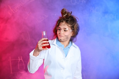 Photo of Emotional pupil holding conical flask in smoke against blackboard with chemistry formulas