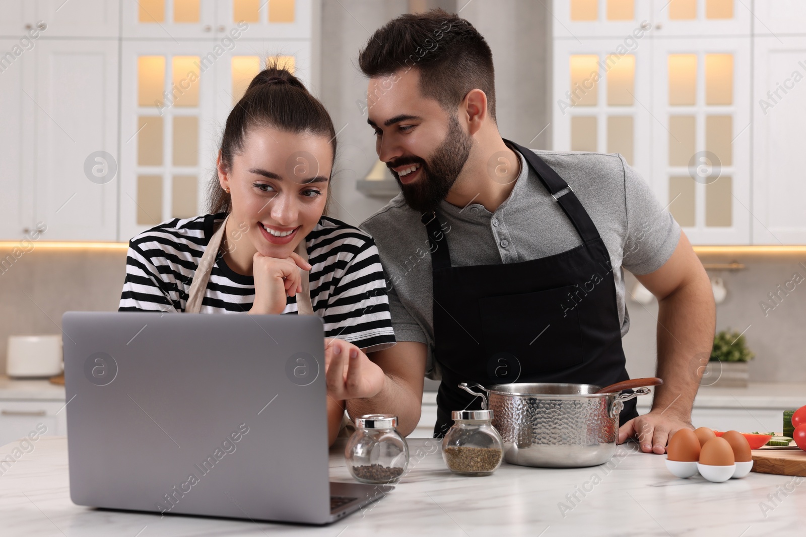 Photo of Happy lovely couple using laptop while cooking in kitchen