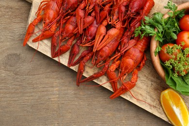 Photo of Delicious red boiled crayfish and products in bowl on wooden table, top view