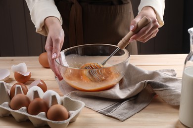 Photo of Woman whisking eggs in bowl at table, closeup