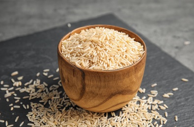 Slate plate with raw unpolished rice in bowl on table