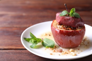 Tasty baked apple with nuts, honey and mint on wooden table, closeup. Space for text