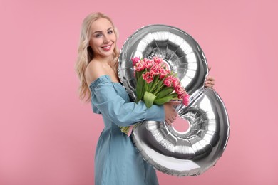 Photo of Happy Women's Day. Charming lady holding bouquet of beautiful flowers and balloon in shape of number 8 on pink background
