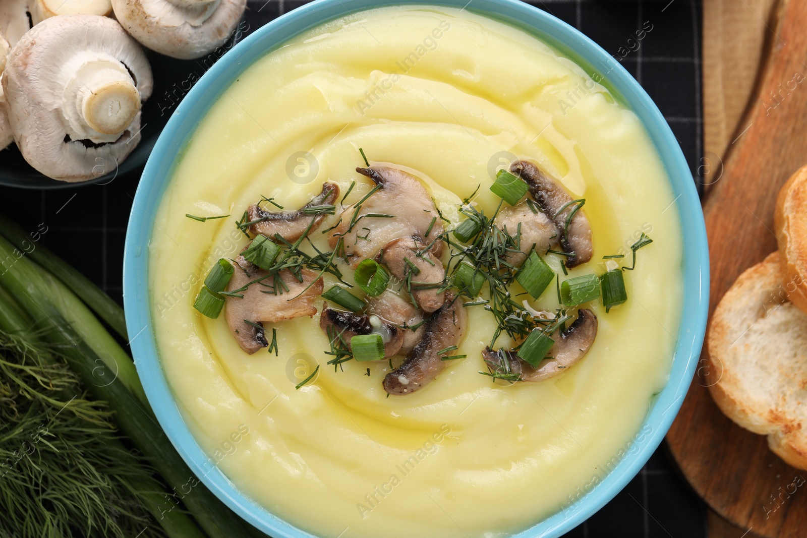 Photo of Bowl of tasty cream soup with mushrooms, green onions and dill on wooden table, flat lay