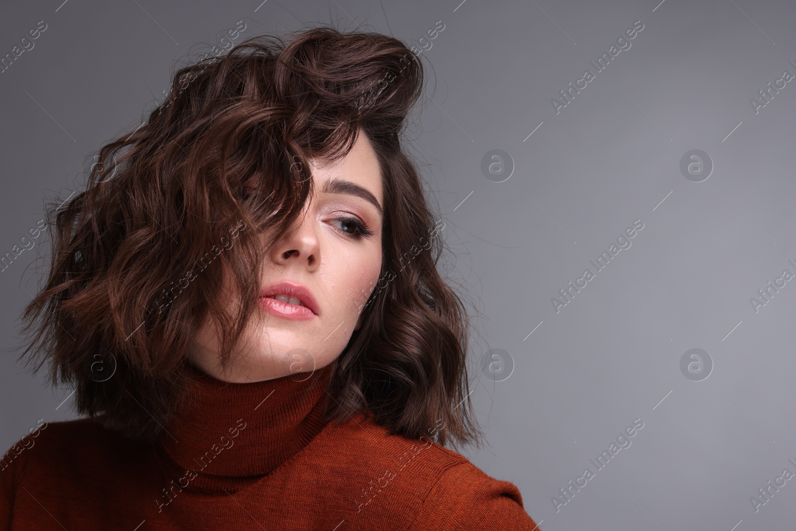 Photo of Portrait of beautiful young woman with wavy hairstyle on grey background. Space for text