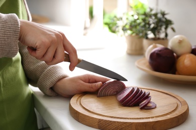 Woman cutting red onion into slices at countertop in kitchen, closeup