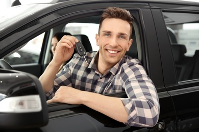 Photo of Young man with key sitting in driver's seat of auto. Buying new car