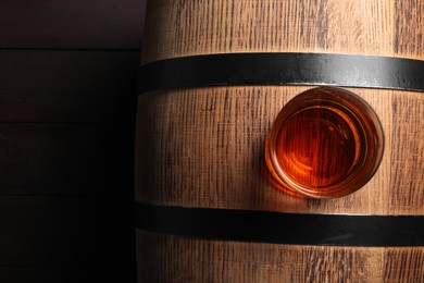 Glass of tasty whiskey on wooden barrel, top view. Space for text