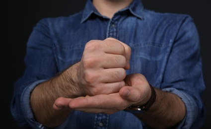Photo of Man showing word CRUCIFY in sign language on black background, closeup