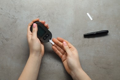 Photo of Diabetes. Woman checking blood sugar level with glucometer at gray table, top view