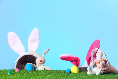 Little girls wearing rabbit ears headbands and playing with toy Easter bunnies on green grass surface against color background