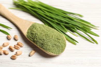 Wheat grass powder in spoon, seeds and fresh sprouts on white wooden table, closeup