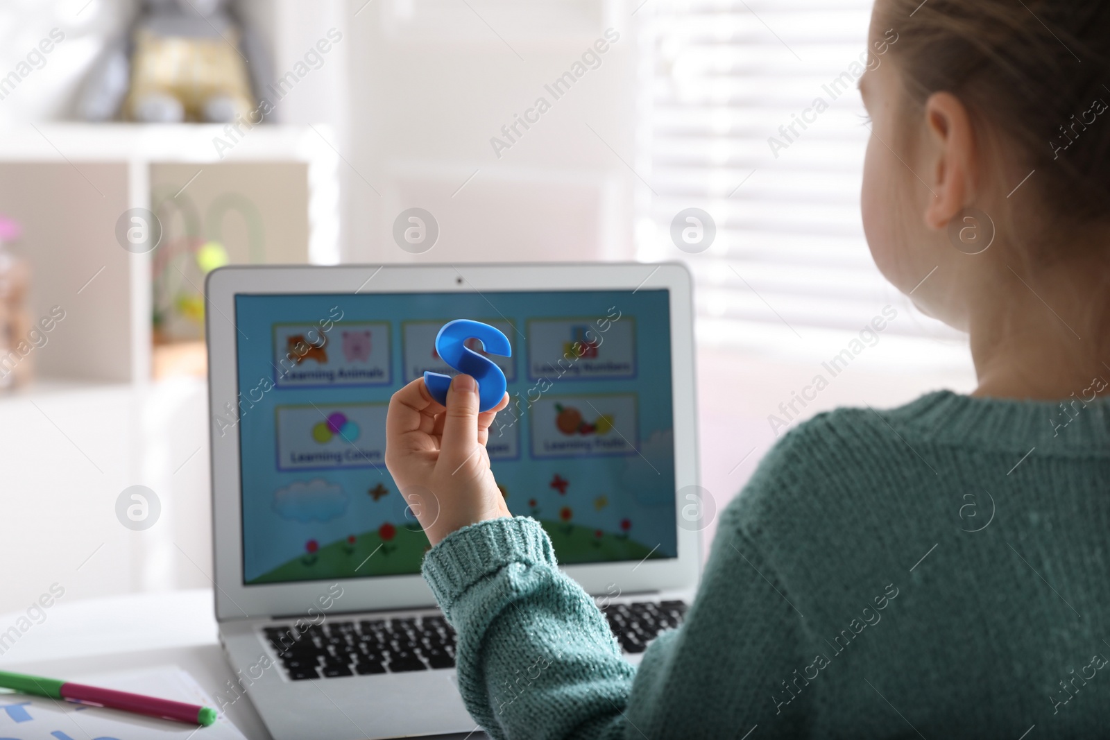 Photo of Little girl learning English indoors at online lesson, closeup