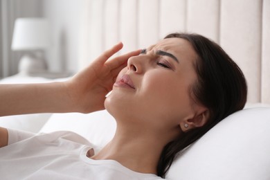 Photo of Young woman suffering from migraine in bed at home