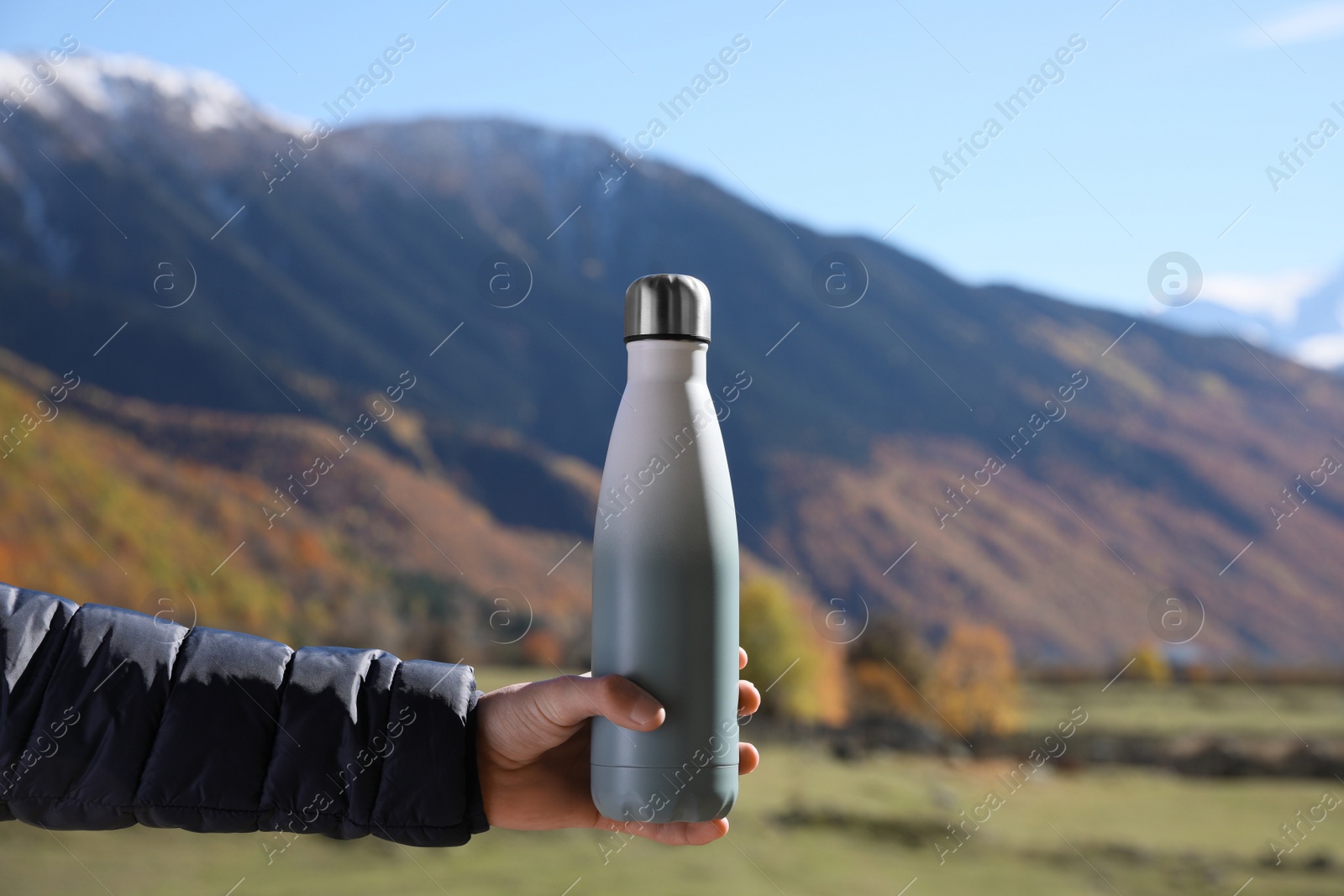 Photo of Boy holding thermo bottle with drink in mountains on sunny day, closeup