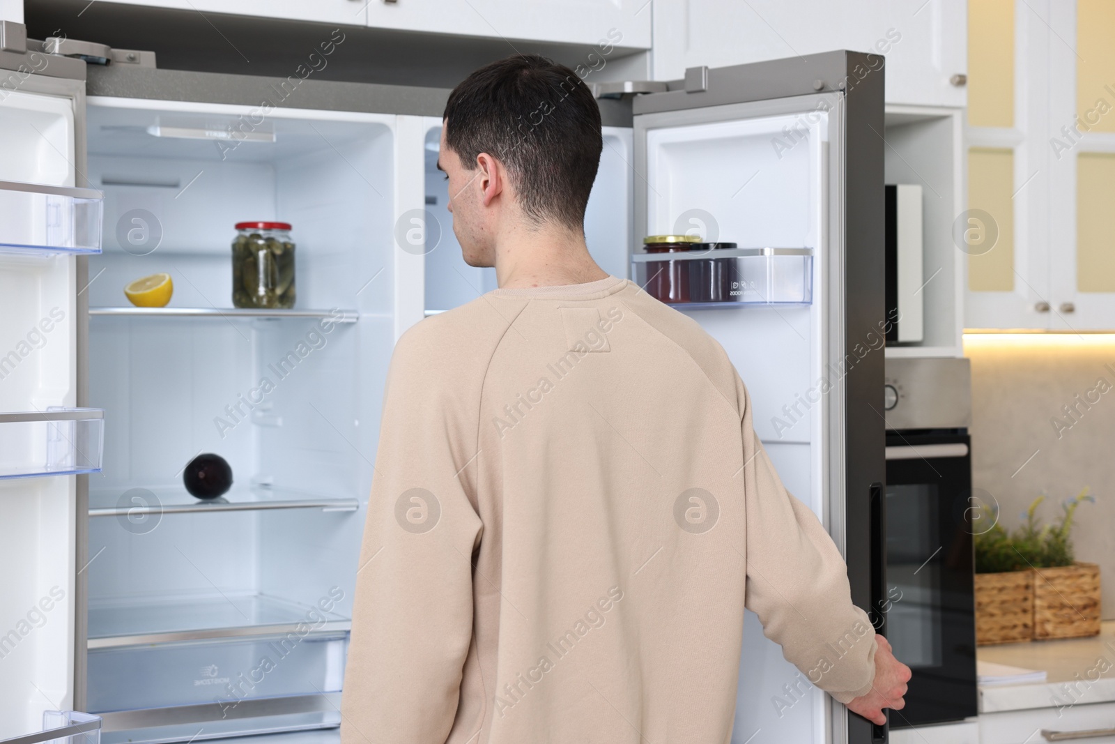 Photo of Man near empty refrigerator in kitchen at home, back view