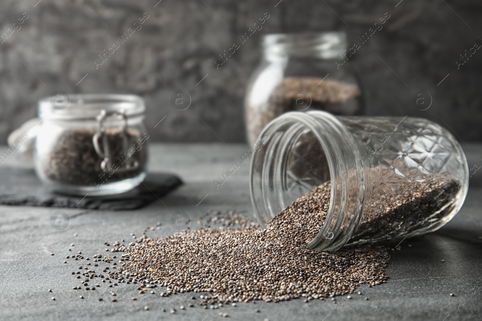 Photo of Glass jar and scattered chia seeds on grey table, space for text