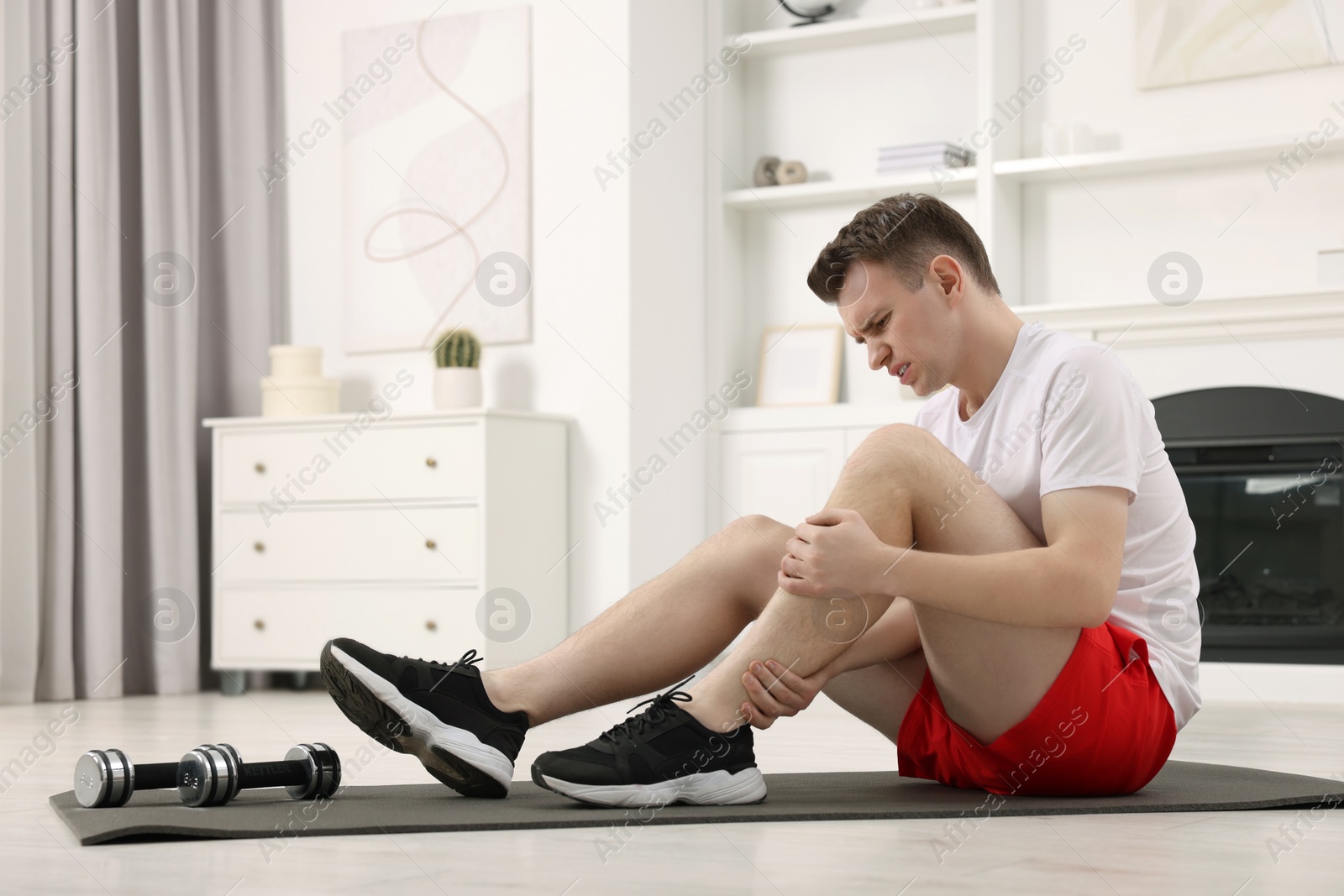 Photo of Man suffering from leg pain on mat at home