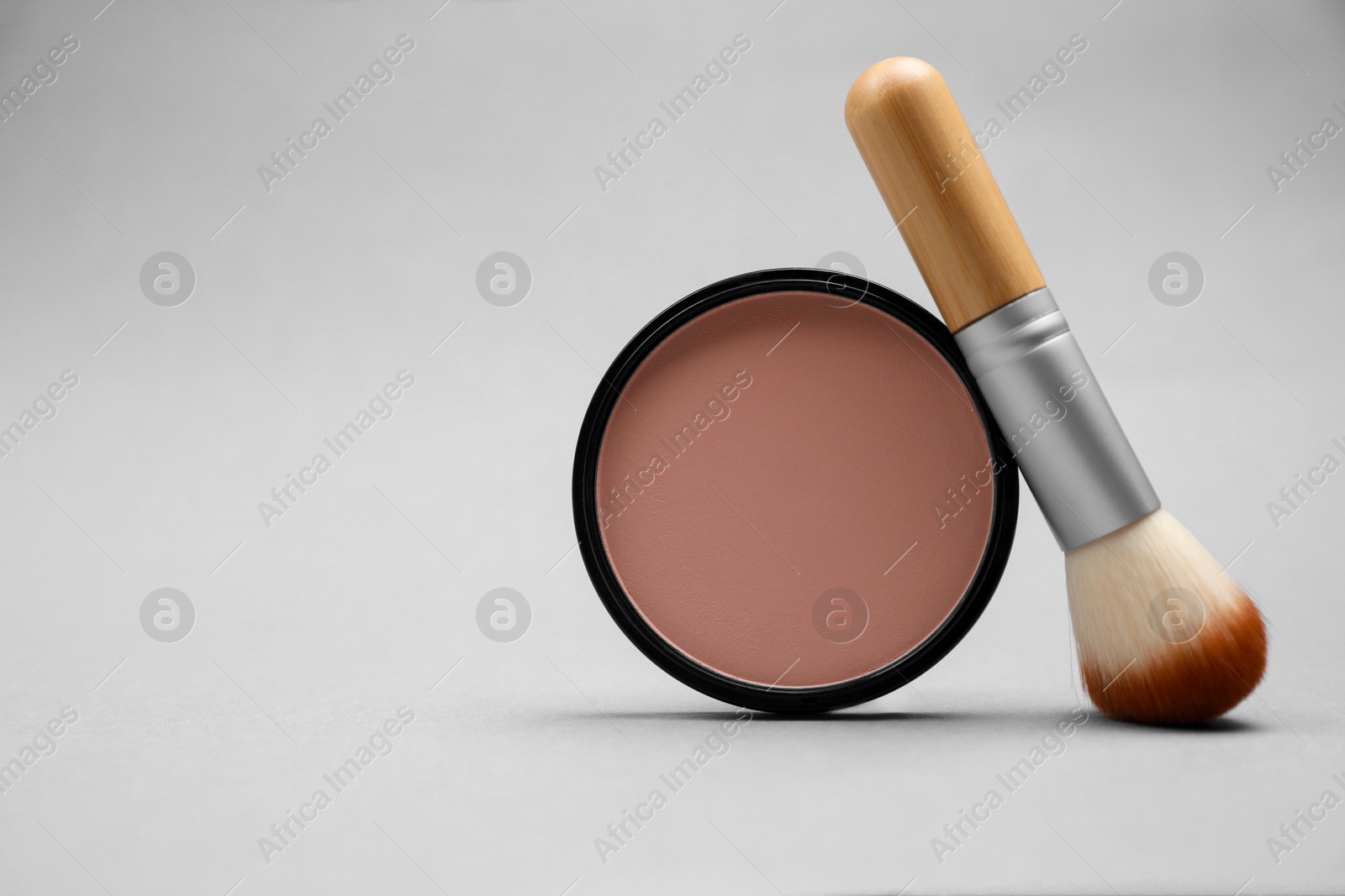 Photo of Open face powder and brush on light grey background. Space for text