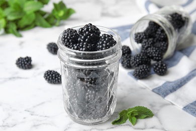 Photo of Glass jars of tasty ripe blackberries on marble table