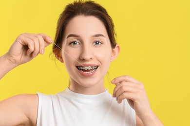 Photo of Smiling woman with braces cleaning teeth using dental floss on yellow background
