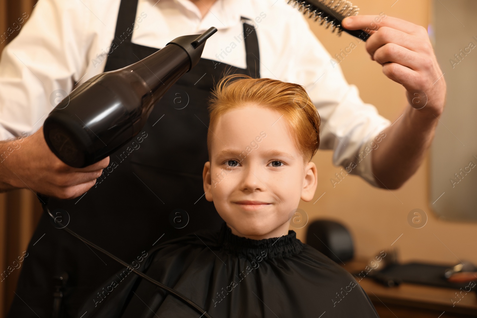 Photo of Professional hairdresser drying boy's hair in beauty salon, closeup