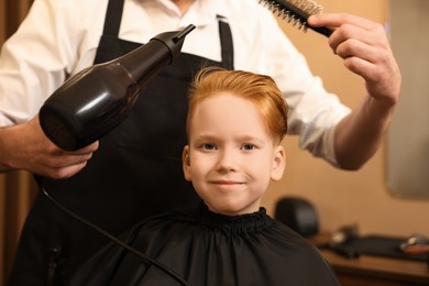 Photo of Professional hairdresser drying boy's hair in beauty salon, closeup