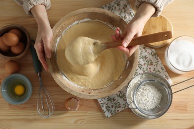 Photo of Woman kneading dough with spoon in bowl at wooden table, top view