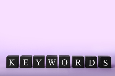 Photo of Black cubes with word KEYWORDS on lilac background