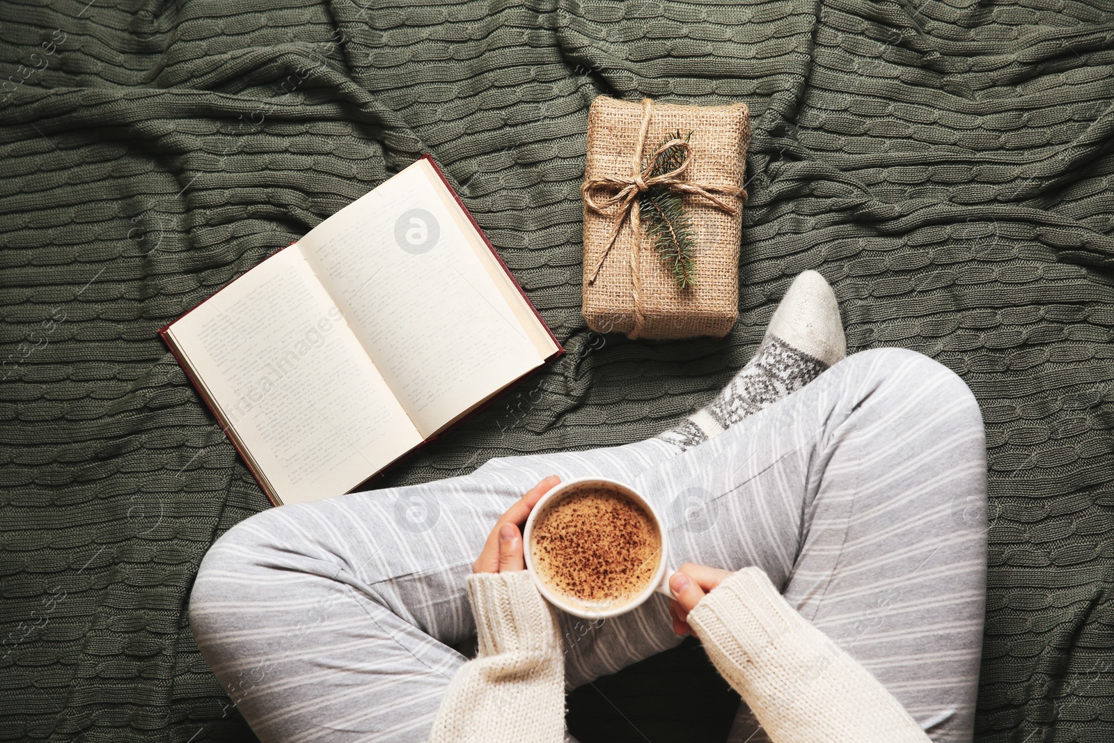 Photo of Woman in knitted socks sitting on warm plaid with hot cocoa, top view