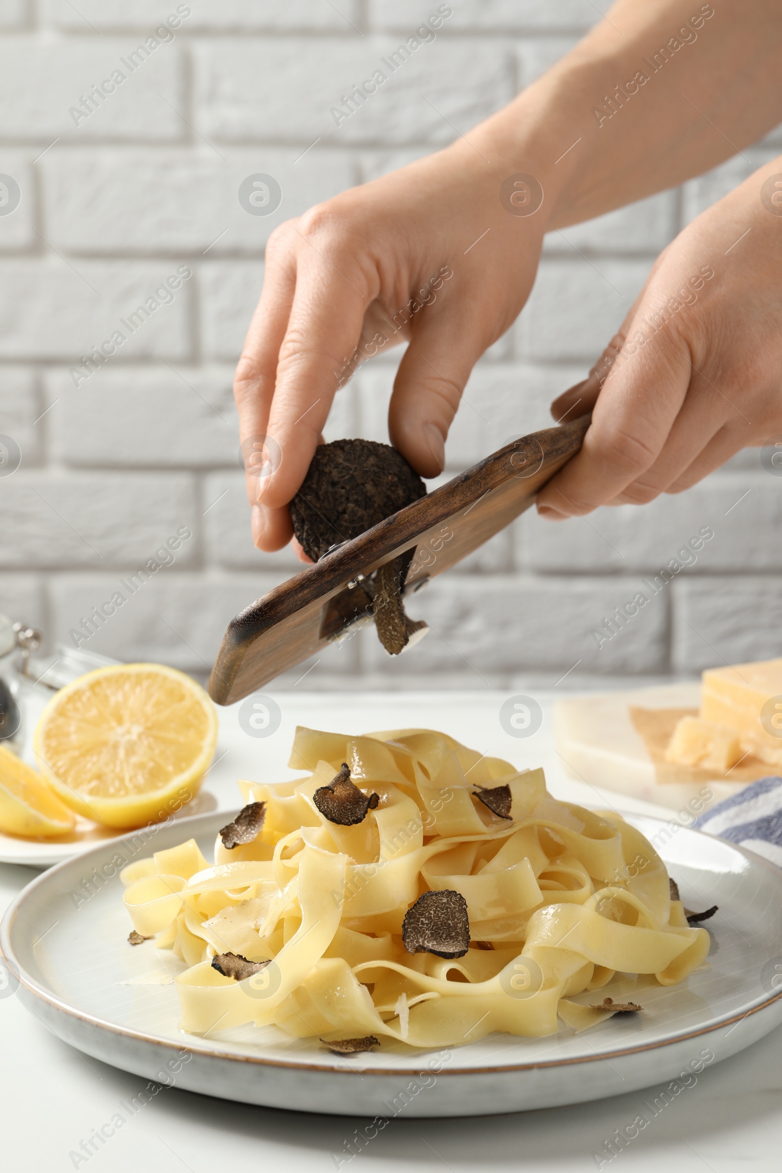 Photo of Woman slicing truffle over delicious pasta at white table, closeup