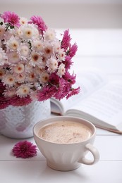 Photo of Cup of fresh coffee, open book and beautiful bouquet on white wooden table near window. Good morning