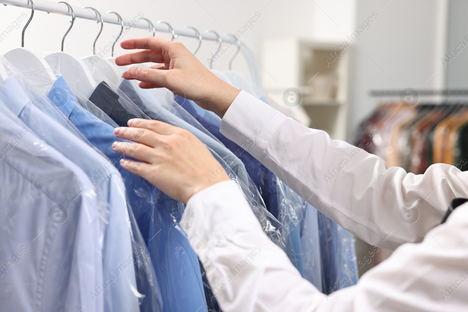 Photo of Dry-cleaning service. Woman taking shirt in plastic bag from rack indoors, closeup