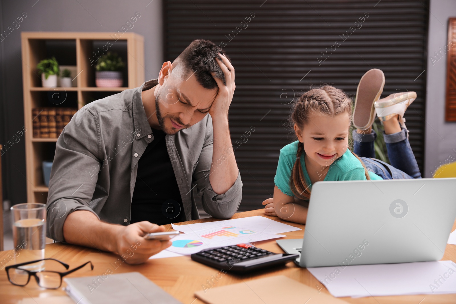 Photo of Overwhelmed man combining parenting and work at home