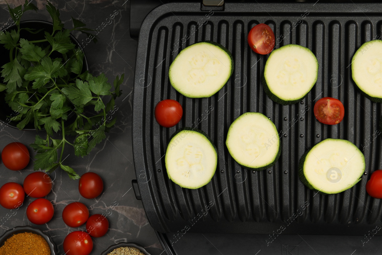 Photo of Electric grill with vegetables on black marble table, flat lay